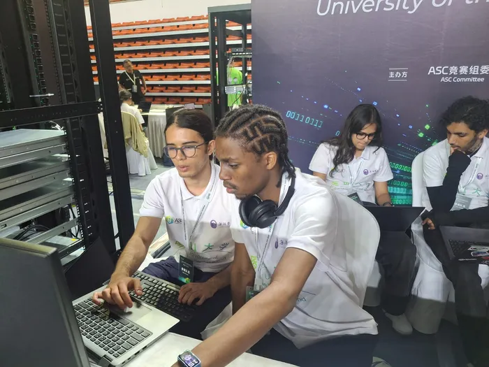 Vele and a teammate working on a laptop beside the cluster racks at the ASC finals.